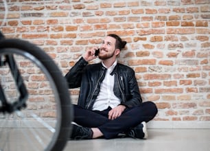 Un joven empresario con bicicleta y teléfono sentado en el suelo de la oficina, haciendo una llamada telefónica.