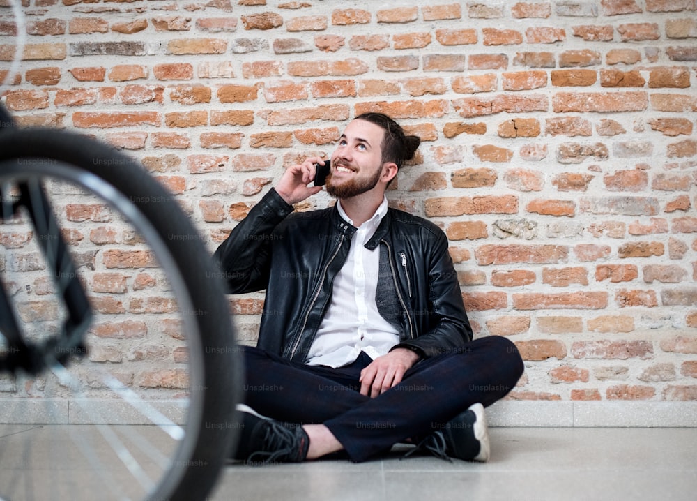 A young businessman with bicycle and telephone sitting on the floor in office, making a phone call.