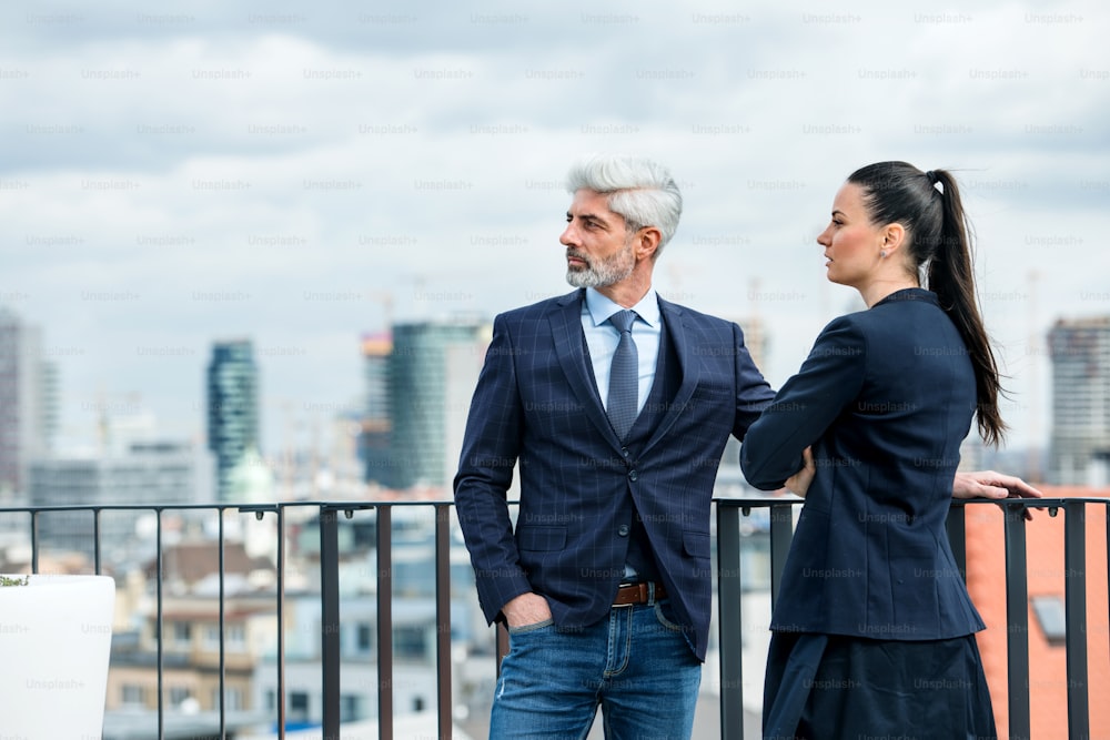 A mature businessman and young businesswoman standing on a terrace, talking.
