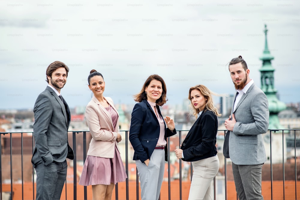 A front view portrait of group of joyful businesspeople standing outdoors on roof terrace in city.