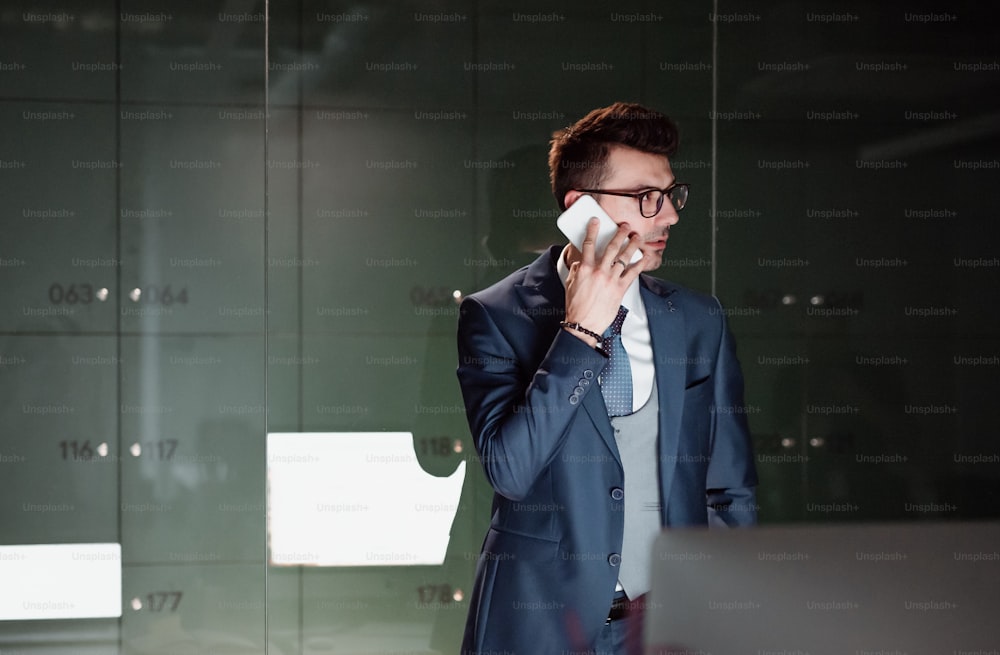 Un portrait d’un jeune homme d’affaires avec un smartphone debout près des casiers dans un bureau, faisant un appel téléphonique. Espace de copie.