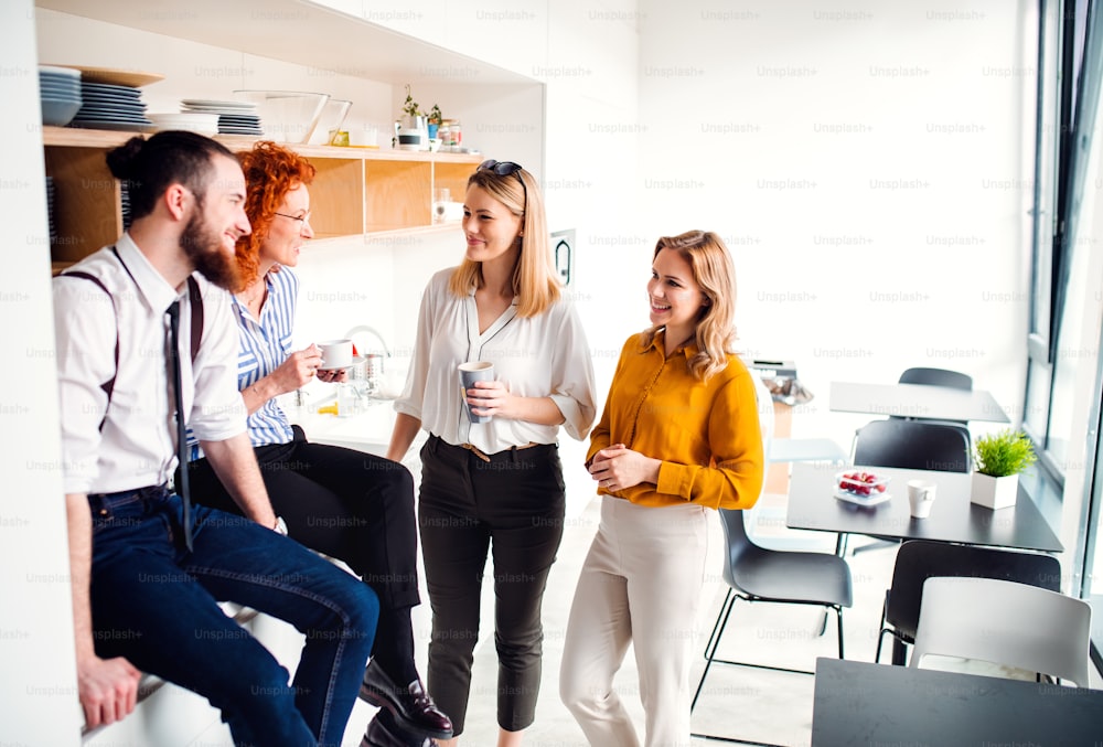 A group of young business people on coffee break in office kitchen, talking.