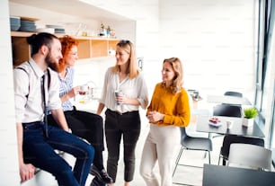 A group of young business people on coffee break in office kitchen, talking.