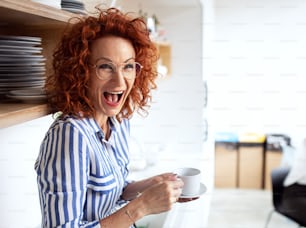 A portrait of joyful businesswoman in an office, holding a cup of coffee and laughing.