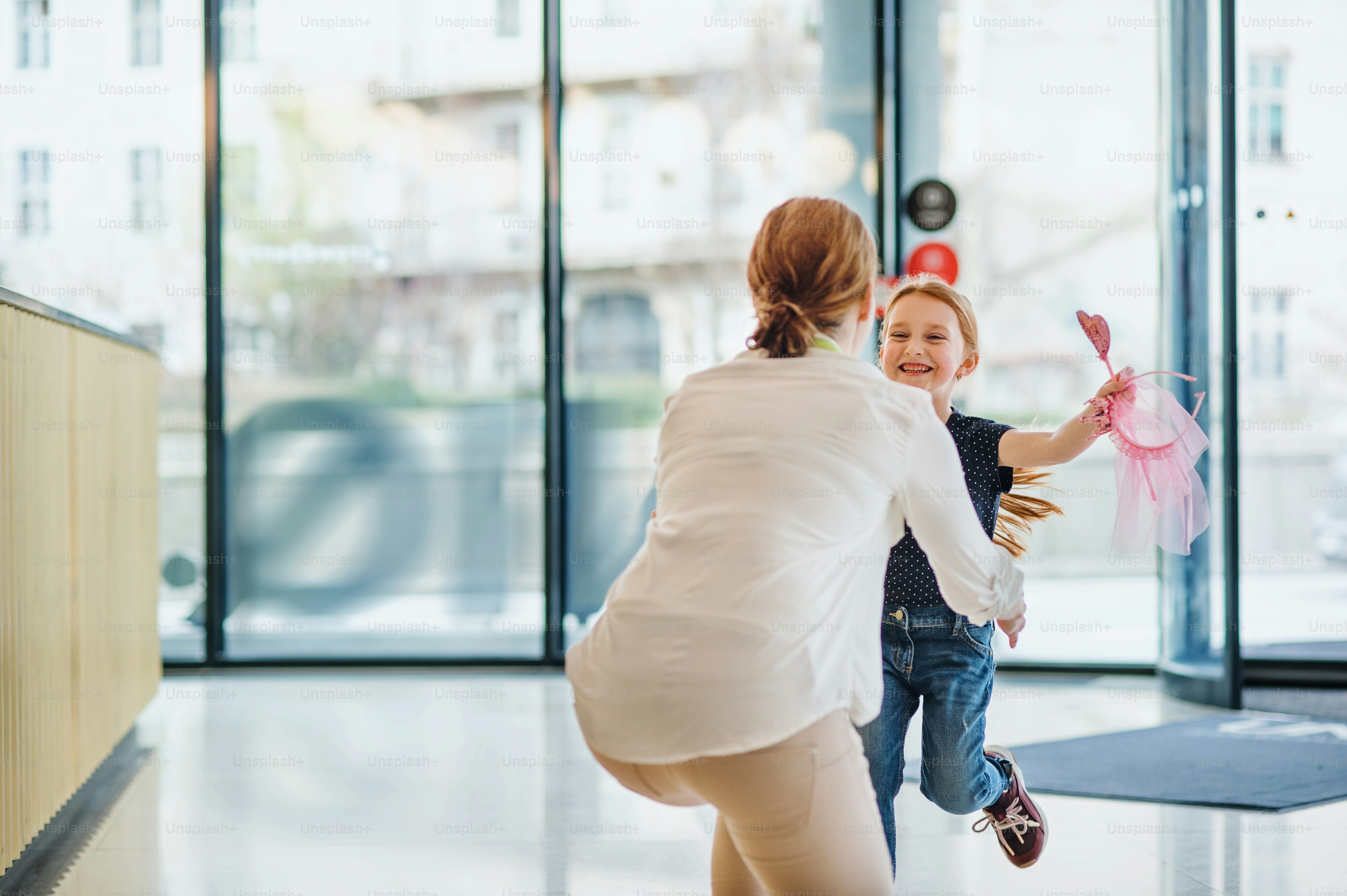 A rear view of businesswoman greeting with happy small daughter in office building.