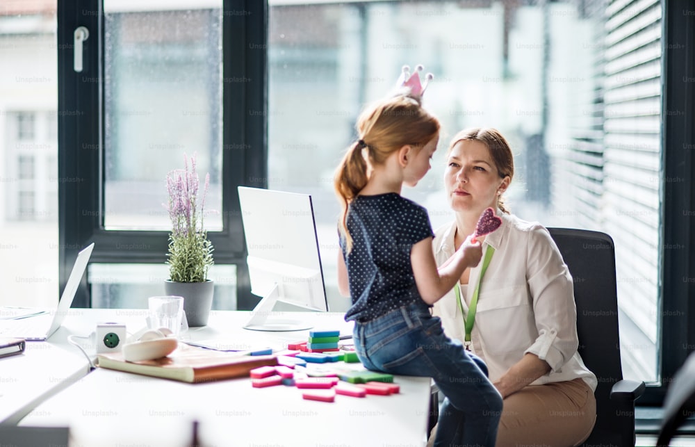 A businesswoman with a small daughter sitting in an office, working.