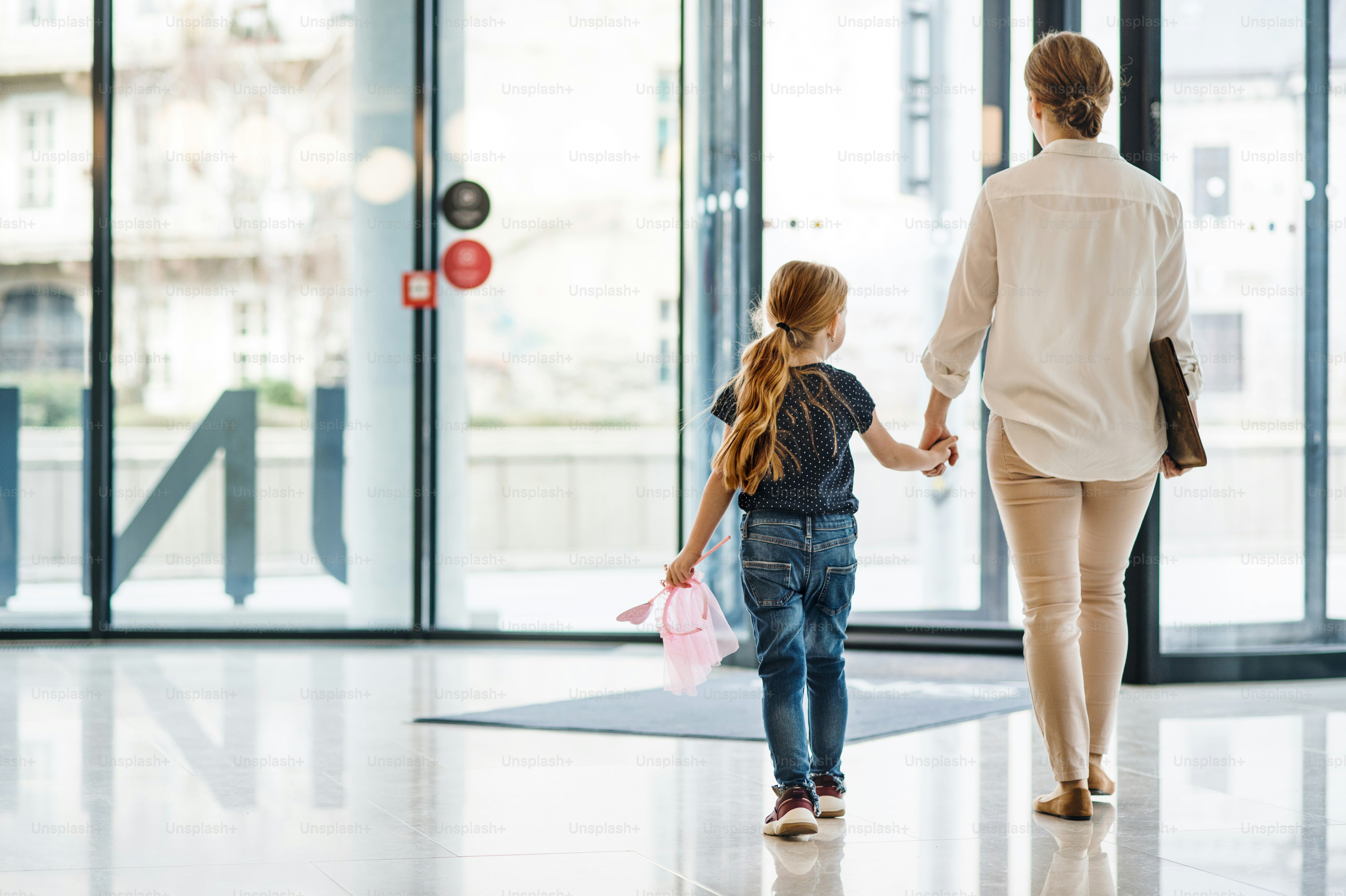 A rear view of businesswoman with small daughter walking in office