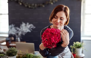 A portrait of young creative woman arranging flowers in a flower shop. A startup of florist business.