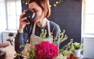Una giovane donna creativa con un caffè che dispone fiori in un negozio di fiori. Una startup di attività di fiorista.