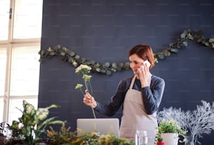 A young creative woman arranging flowers in a flower shop, using smartphone. A startup of florist business.