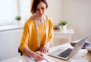 Giovane donna creativa con il computer portatile che lavora in uno studio, avvio di una piccola sartoria.
