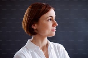 Ein Nahaufnahmeporträt einer jungen schönen Frau, die vor dunklem Hintergrund steht.