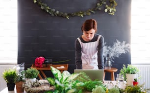 Uma jovem mulher criativa organizando flores em uma floricultura, usando laptop. Uma startup de negócios de floristas.