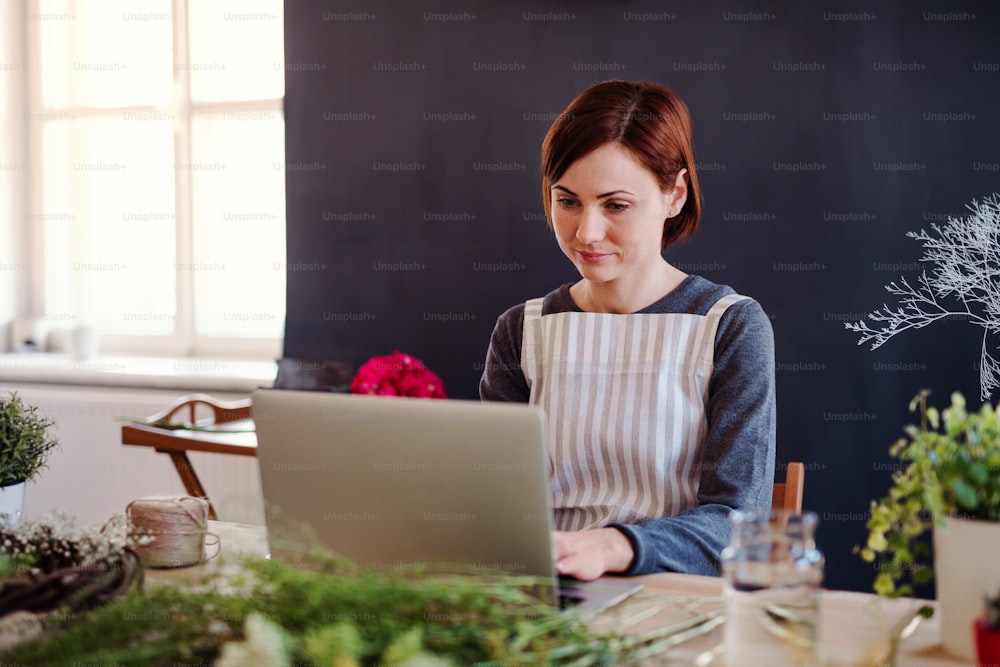 Uma jovem mulher criativa organizando flores em uma floricultura, usando laptop. Uma startup de negócios de floristas.
