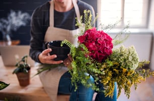 Ein Mittelteil einer jungen kreativen Frau mit einem Kaffee, die Blumen in einem Blumenladen arrangiert. Ein Startup des Floristengeschäfts.