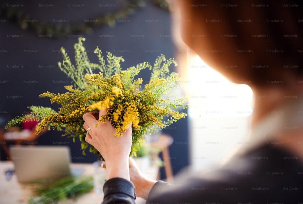 Una sezione intermedia di una giovane donna creativa che organizza fiori in un negozio di fiori. Una startup di attività di fiorista. Veduta posteriore.