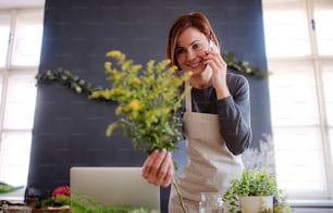 A young creative woman arranging flowers in a flower shop, using smartphone. A startup of florist business.