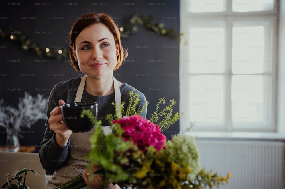 꽃집에서 꽃꽂이를 하는 커피를 들고 있는 젊은 창조적인 여성. 플로리스트 사업의 창업.
