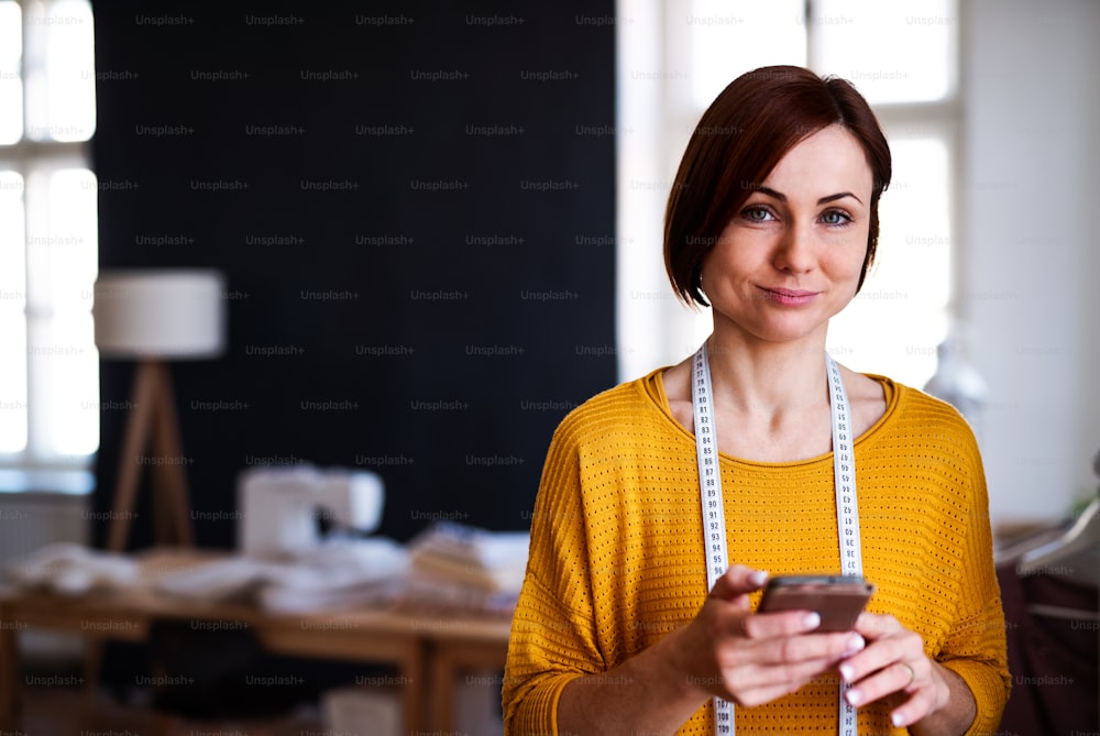 Young creative woman in a studio, using smartphone. A startup of small tailoring business. Copy space.