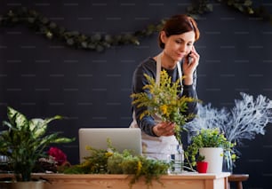 A young creative woman arranging flowers in a flower shop, using smartphone. A startup of florist business.