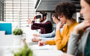 A group of young businesspeople with computers and VR goggles working together in office. Copy space.