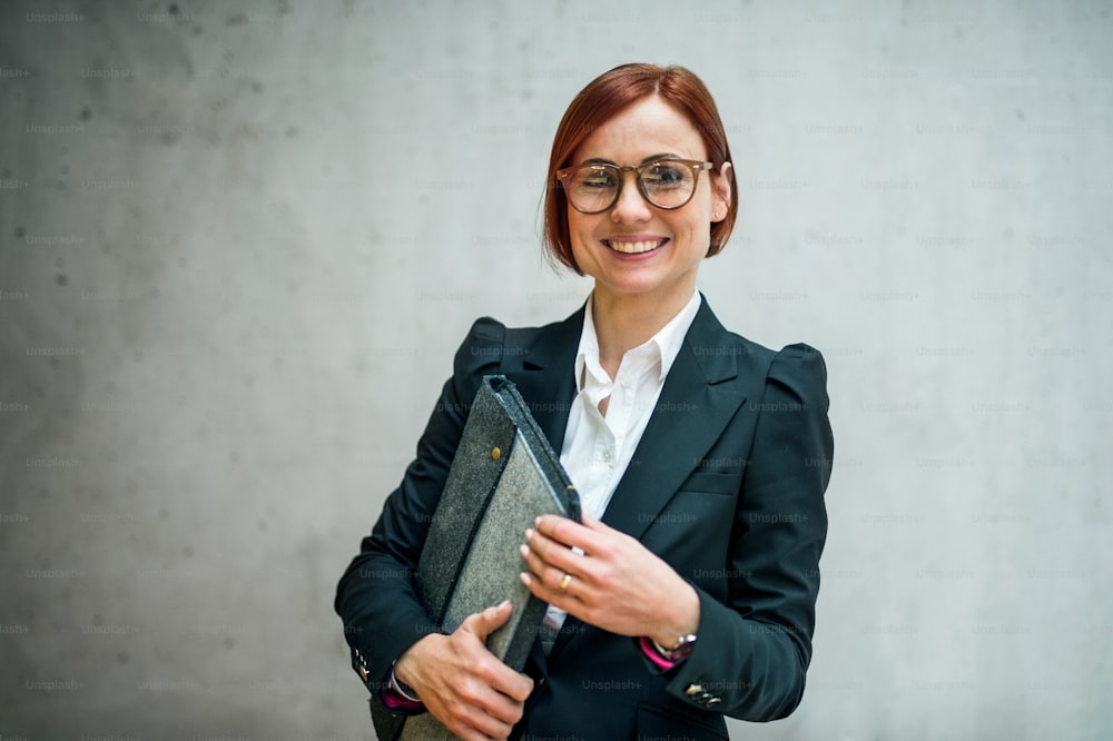 Ein Porträt einer jungen fröhlichen Geschäftsfrau, die im Büro steht und in die Kamera schaut.
