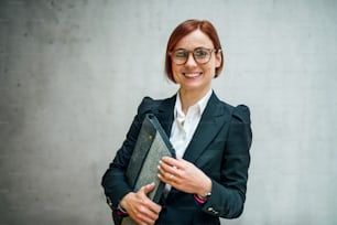 A portrait of young cheerful businesswoman standing in office, looking at camera.
