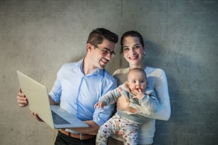 Um jovem empresário com esposa e filha bebê juntos no escritório, usando laptop.