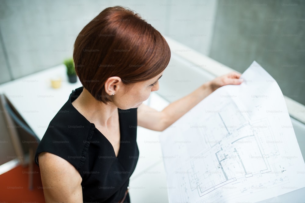 Une jeune femme d’affaires ou un architecte debout dans un bureau, regardant des plans.