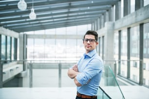 A portrait of young businessman standing indoors in an office, arms crossed. Copy space.