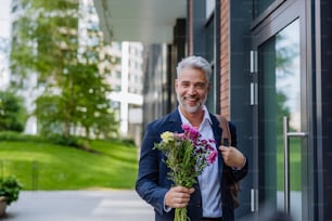 A portrait of happy mature businessman with flower bouquet walking in street to meet his girlfriend.