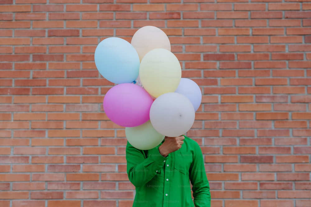 A fun portrait of happy energetic mature man holding balloons in street and hiding behind them, feeling free.