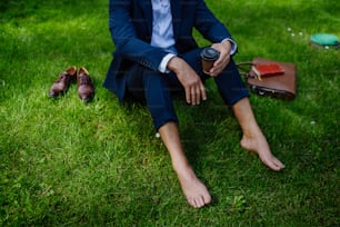 Un hombre de negocios tomando café, descansando y sentado descalzo en el parque, sintiéndose libre, escapando del trabajo, concepto de equilibrio entre la vida laboral y personal.