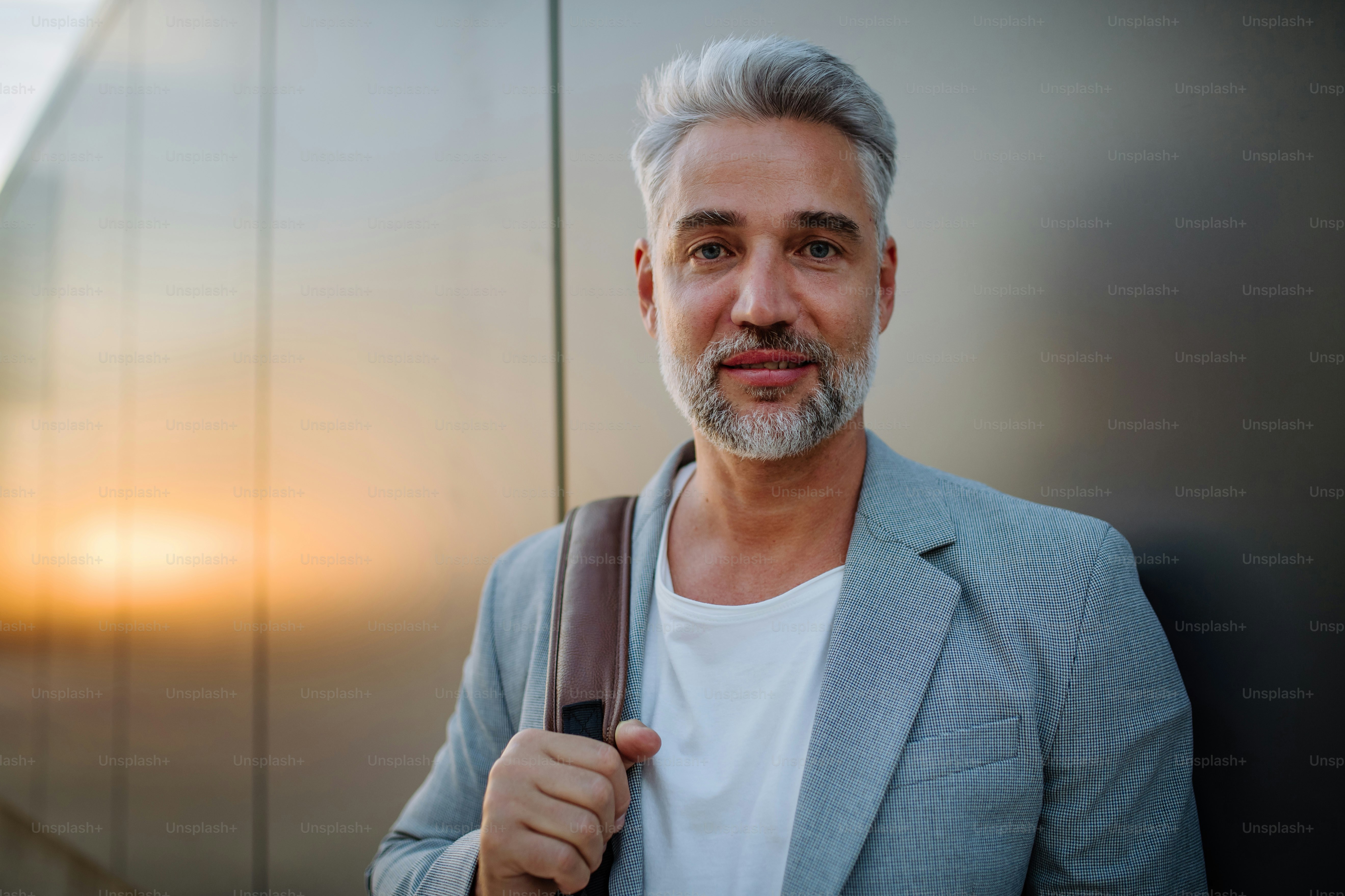 A mature relaxed businessman leaning on street wall and looking at camera, work life balance concept.