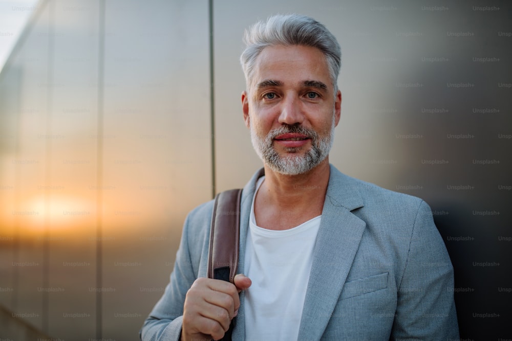 A mature relaxed businessman leaning on street wall and looking at camera, work life balance concept.