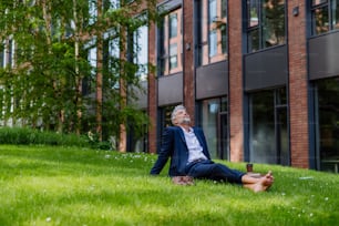 Un uomo d'affari maturo che riposa e siede a piedi nudi nel parco, sentendosi libero, fuggendo dal lavoro, concetto di equilibrio tra lavoro e vita privata.