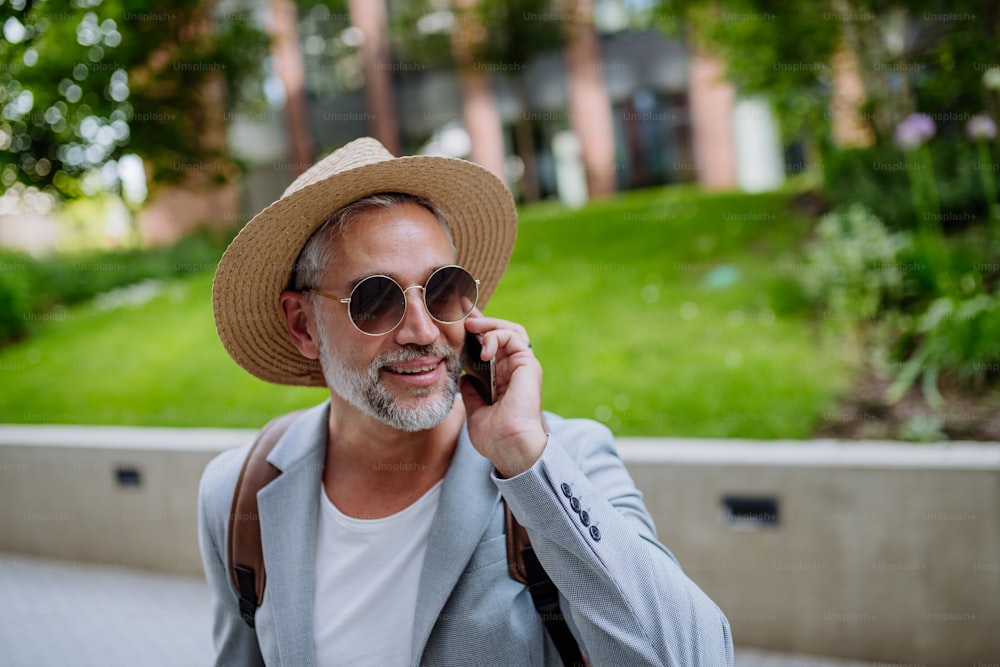 A confident man wearing straw hat and backpack talking on phone, businessman in casual clothes in summer on the way to work.