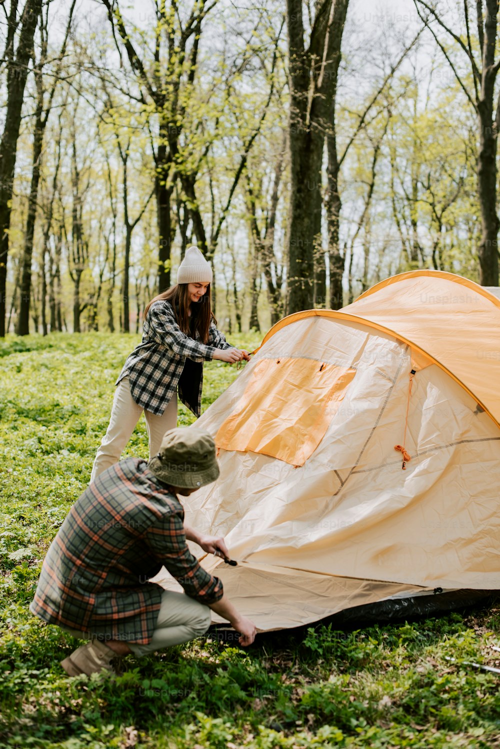 two people setting up a tent in the woods