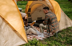 a man and woman sitting in a tent reading a book