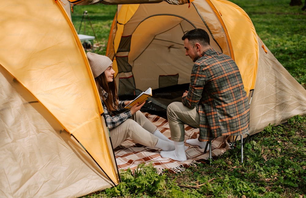 a man and woman sitting in a tent reading a book