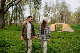 a man and a woman standing in a field with a tent in the background