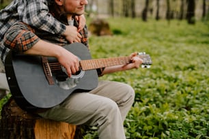 a man sitting on a tree stump playing a guitar