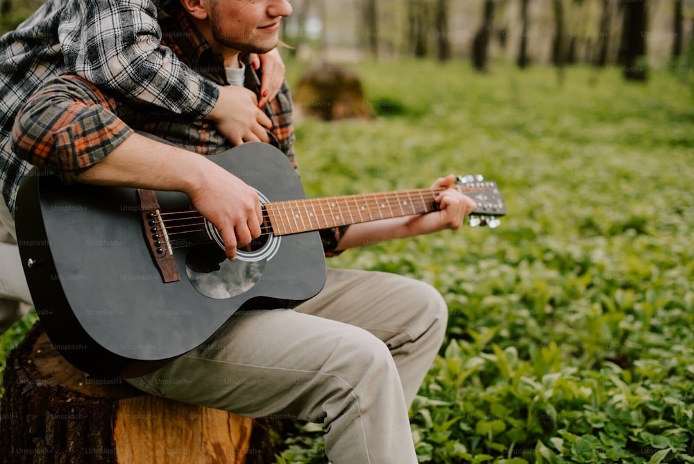 a man sitting on a tree stump playing a guitar