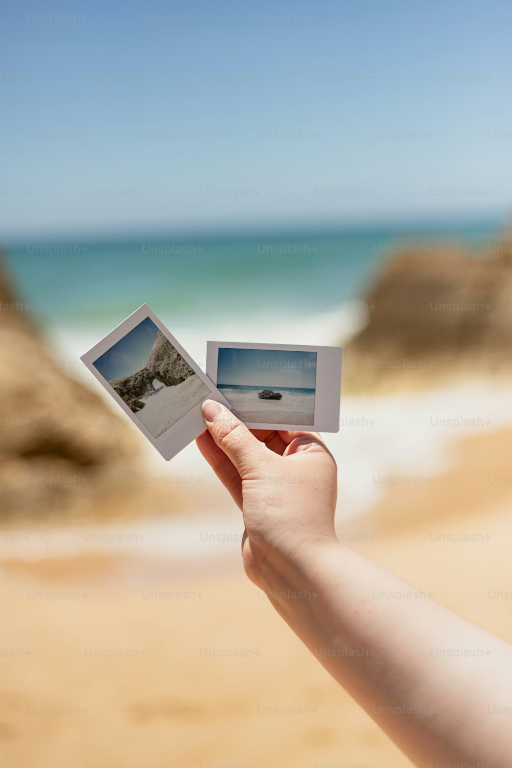 Eine Hand, die ein Polaroid mit einem Strand im Hintergrund hält