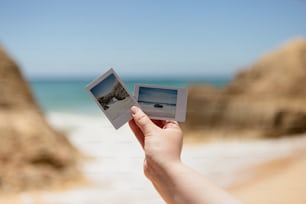 Eine Hand, die ein Polaroid mit einem Strand im Hintergrund hält