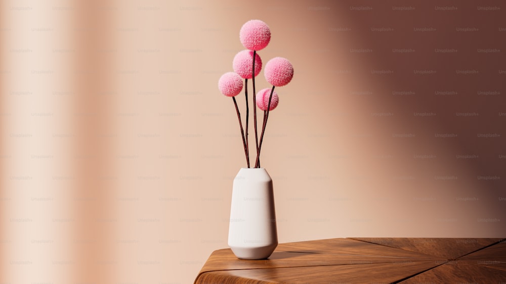 a white vase filled with pink flowers on top of a wooden table