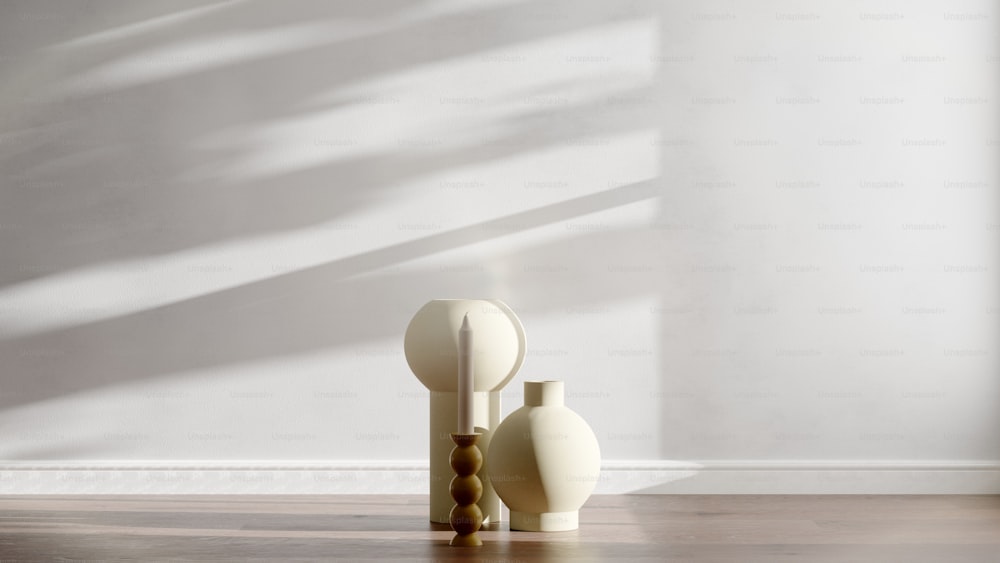 two white vases on a wooden floor in front of a white wall