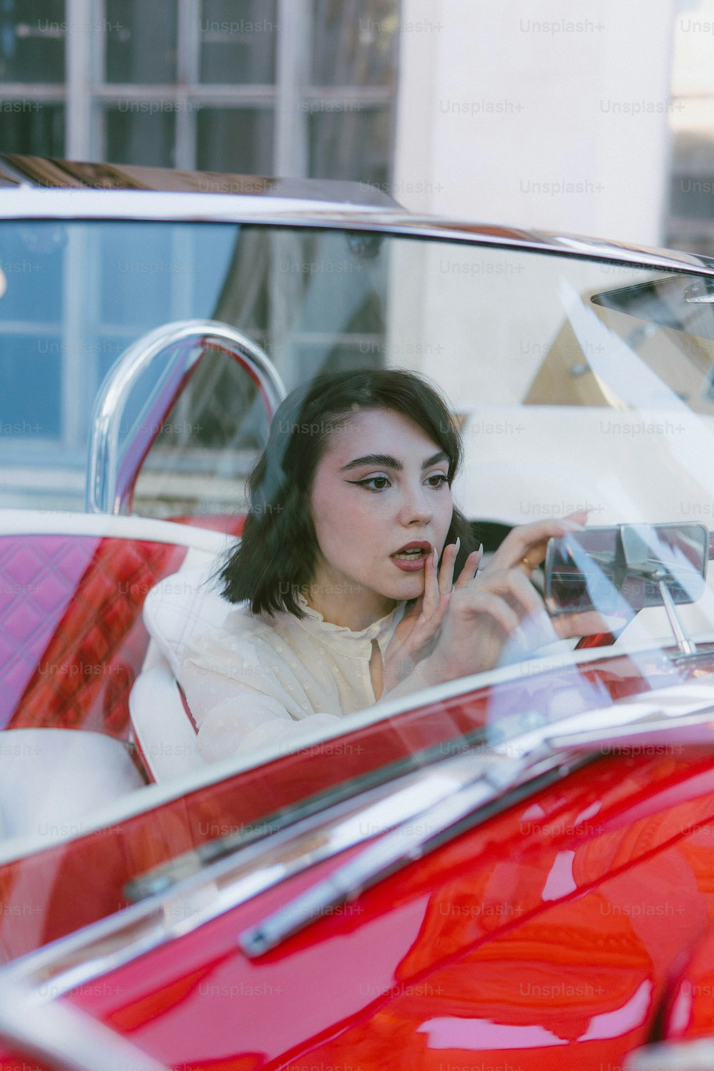 a woman sitting in a red car smoking a cigarette