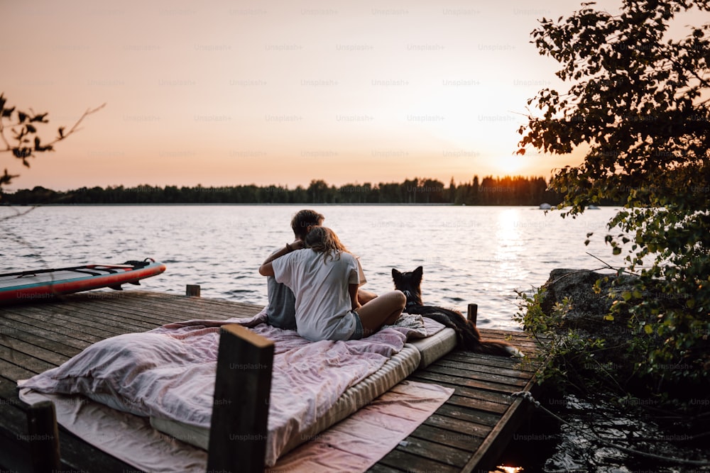 a man and a woman sitting on a dock with a cat