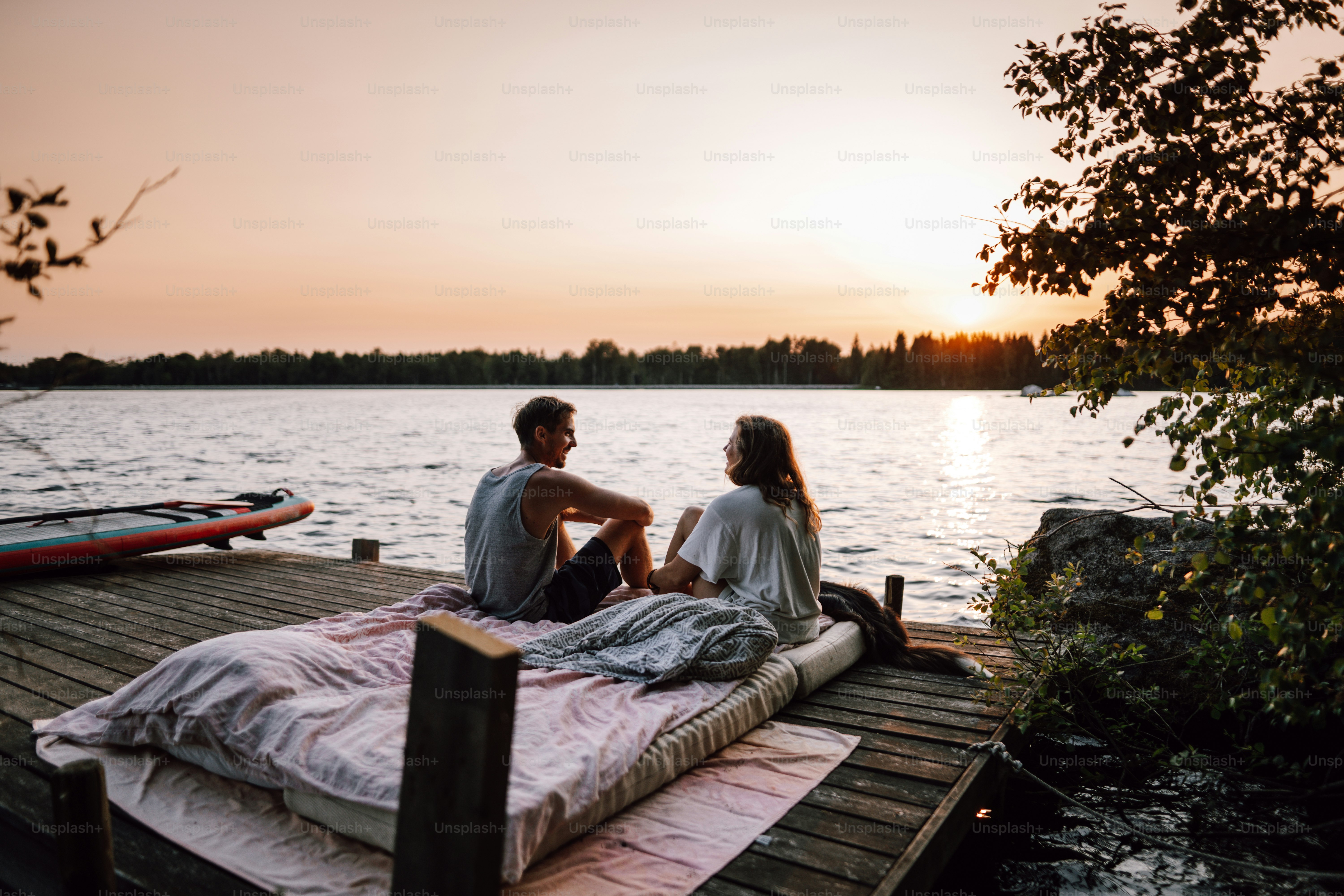 a man and a woman sitting on a dock next to a body of water